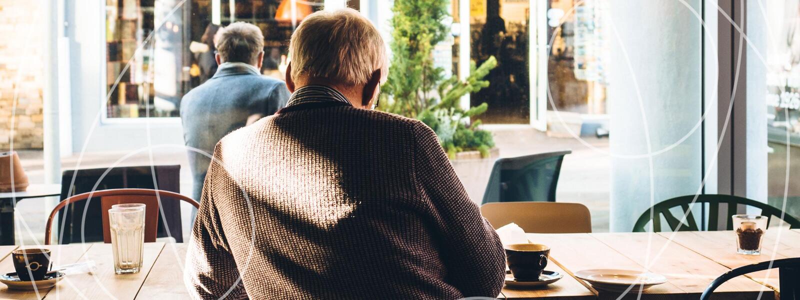 older man's back turned to viewer, studying and reading in coffee shop 
