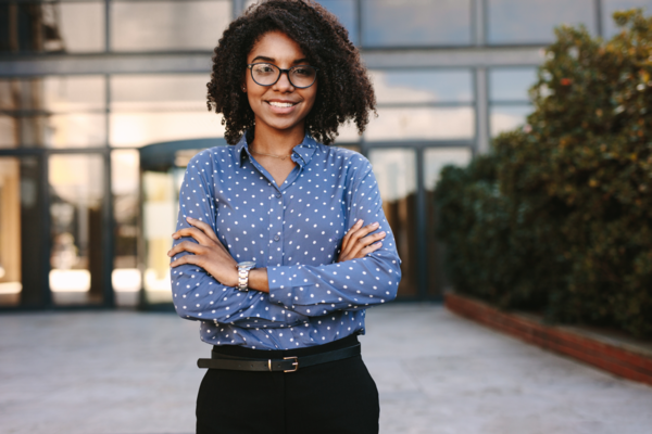 A person wearing business attire and glasses smiles while standing in front of a corporate building. 