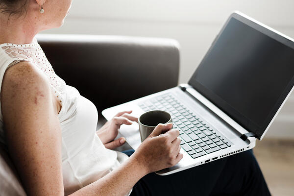 woman holding mug and computer on couch